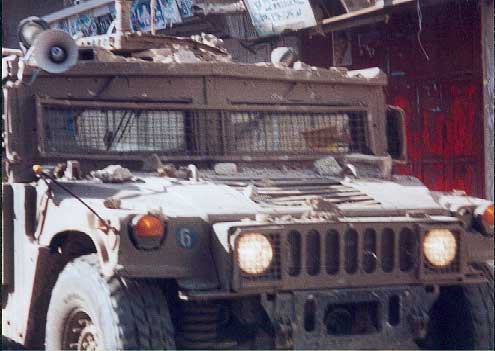 Hummer armored car drives through  Balata Camp covered in stones.